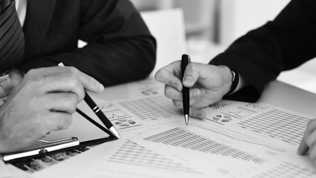 Two people in suits reviewing printed financial charts and graphs at a table